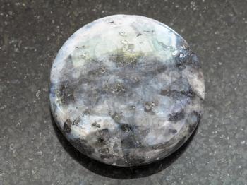 macro shooting of natural mineral rock specimen - bead from gray Labradorite gemstone on dark granite background
