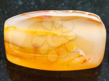 macro shooting of natural mineral rock specimen - cabochon from yellow Agate gemstone on dark granite background