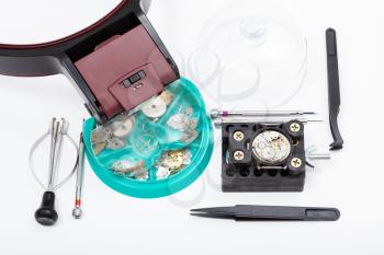 watchmaker workshop - above view of set of tools with head-mounted magnifier and spare parts for repairing mechanical watch on white background