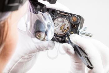 watchmaker workshop - watchmaker in head-mounted magnifier repairs old mechanical watch with tweezers