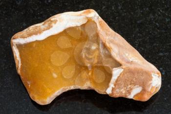 macro shooting of natural mineral rock specimen - pebble of yellow Flint stone on dark granite background