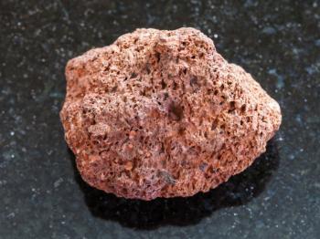 macro shooting of natural mineral rock specimen - tumbled red pumice stone on dark granite background from Sicily