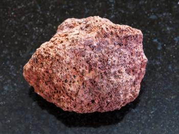macro shooting of natural mineral rock specimen - pebble of red pumice stone on dark granite background from Sicily