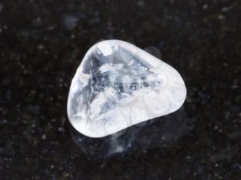 macro shooting of natural mineral rock specimen - tumbled rock crystal gemstone on dark granite background