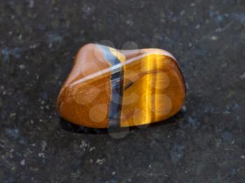 macro shooting of natural mineral rock specimen - tumbled tiger eye gemstone on dark granite background from South Africa
