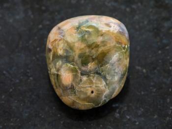macro shooting of natural mineral rock specimen - tumbled rhyolite rainforest jasper gemstone on dark granite backgroundte background