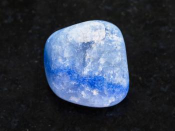 macro shooting of natural mineral rock specimen - tumbled blue dyed agate gemstone on dark granite background