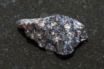 macro shooting of natural mineral rock specimen - rough obsidian (volcanic glass) stone on dark granite background
