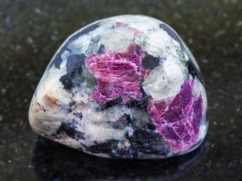 macro shooting of natural mineral stone specimen - tumbled pink Corundum crystals in rock on dark granite background