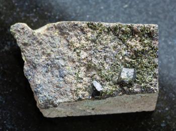 macro shooting of natural mineral stone specimen - raw green crystals of Epidote on rock on dark granite background from Irkutsk region, Russia