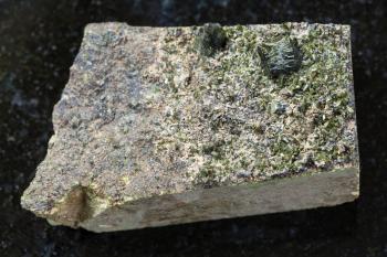 macro shooting of natural mineral stone specimen - rough crystals of Epidote on rock on dark granite background from Irkutsk region, Russia