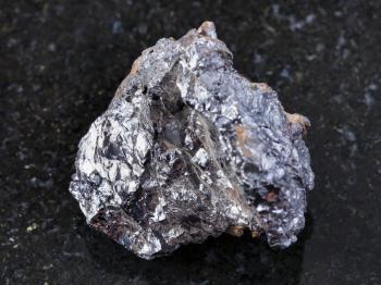 macro shooting of natural mineral rock specimen - raw ilmenorutile (Nb-bearing rutile) stone on dark granite background from South Ural Mountains, Russia