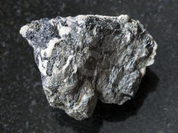 macro shooting of natural mineral rock specimen - rough Knopite stone on dark granite background from Afrikanda district, Kola Peninsula, Russia
