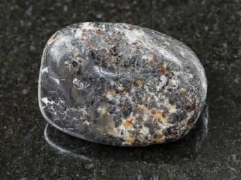 macro shooting of natural mineral rock specimen - polished magnetite stone on dark granite background from Kovdor district of Kola Peninsula, Russia