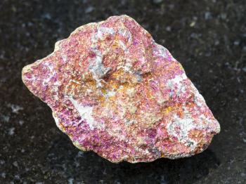 macro shooting of natural mineral rock specimen - raw red Chalcopyrite stone on dark granite background from Mexico