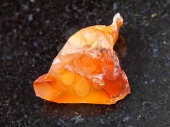macro shooting of natural mineral rock specimen - crystal of Carnelian (red chalcedony) gemstone on dark granite background from Zeya River region in the Russian Far East