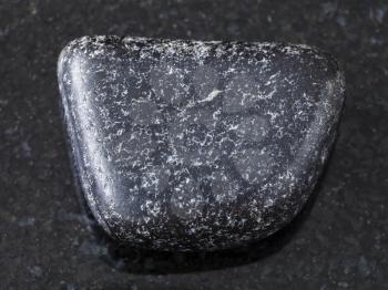 macro shooting of natural mineral rock specimen - tumbled Chromite stone on dark granite background from Saranovskoe mine, Ural Mountains, Russia