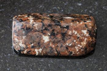 macro shooting of natural mineral rock specimen - polished spreusteined urtite stone on dark granite background from Khibiny Mountains, Kola Peninsula, Russia