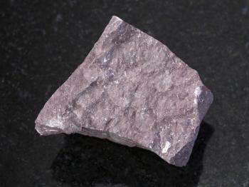 macro shooting of natural mineral rock specimen - rough Aleurolite stone on dark granite background