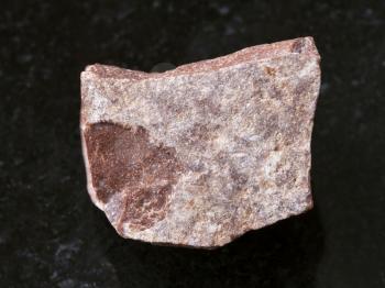 macro shooting of natural mineral rock specimen - piece of raw red marble stone on dark granite background