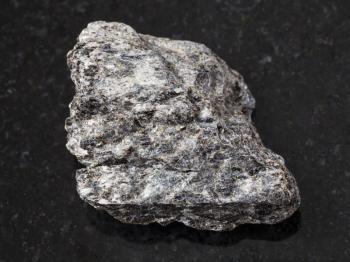 macro shooting of natural mineral rock specimen - rough quartz-biotite schist stone on dark granite background