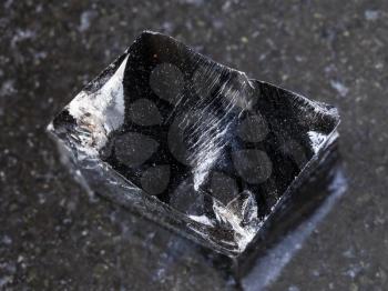 macro shooting of natural mineral rock specimen - piece of rough Obsidian (volcanic glass) stone on dark granite background