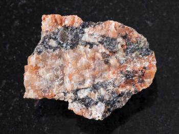 macro shooting of natural mineral rock specimen - rough red granite stone on dark granite background