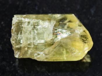 macro shooting of natural mineral rock specimen - crystal of yellow apatite gemstone on dark granite background from Mexico