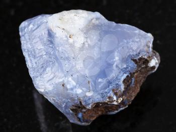 macro shooting of natural mineral rock specimen - rough crystal of blue Chalcedony gemstone on dark granite background from Transbaikalia (Zabaykalye), Russia