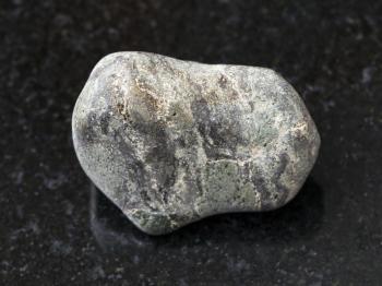 macro shooting of natural mineral rock specimen - tumbled Suevite stone on dark granite background from Karelia, Rissia