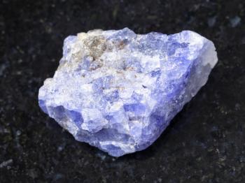 macro shooting of natural mineral rock specimen - rough crystal of Tanzanite gemstone on dark granite background from Tanzania