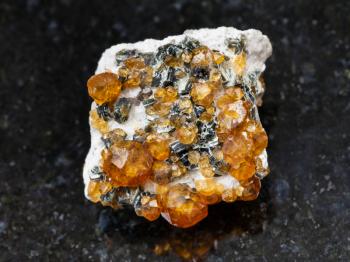 macro shooting of natural mineral rock specimen - raw crystals of spessartine gemstone on dark granite background from Fujian region, China