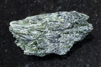 macro shooting of natural mineral rock specimen - raw Actinolite stone on dark granite background from Verkhny Ufaley district, Ural, Russia