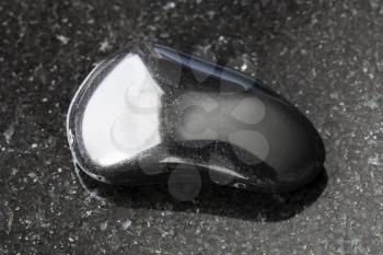 macro shooting of natural mineral rock specimen - polished black obsidian gemstone on dark granite background from Mexico