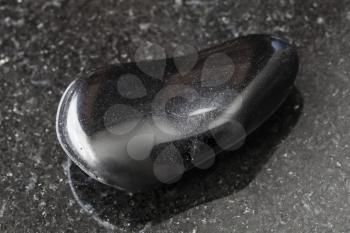 macro shooting of natural mineral rock specimen - tumbled black obsidian gemstone on dark granite background from Mexico