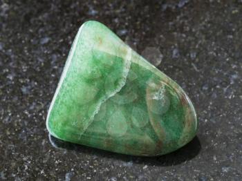 macro shooting of natural mineral rock specimen - polished green aventurine gem stone on dark granite background from Zimbabwe