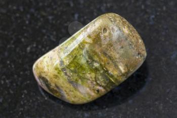 macro shooting of natural mineral rock specimen - tumbled unakite gem stone on dark granite background from South Africa