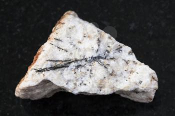 macro shooting of natural mineral rock specimen - black Ludwigite crystals in rough stone on dark granite background from Praskovie-Evgenyevskaya mine, South Ural, Russia