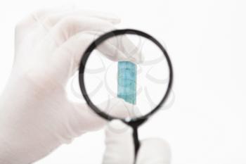 master checks aquamarine crystal with magnifier on white background
