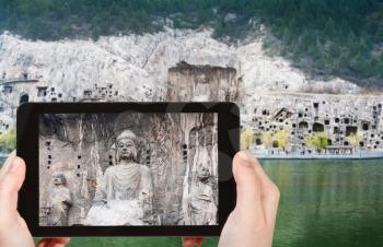 travel concept - tourist photographs Buddha statue on West Hill of Chinese Buddhist monument Longmen Grottoes (Longmen Caves) from the east bank of the Yi River in spring season on tablet