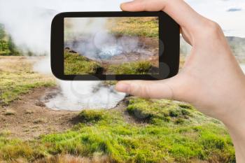travel concept - tourist photographs geyser in Haukadalur hot spring area in Iceland in september on smartphone