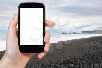 travel concept - tourist photographs Reynisfjara Beach and view of Dyrholaey promontory in Iceland on Atlantic South Coast in autumn on smartphone with cut out screen for advertising logo