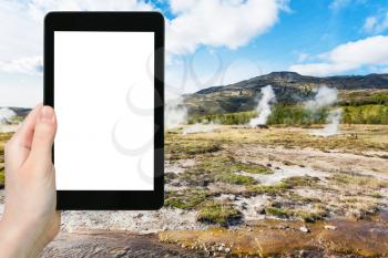travel concept - tourist photographs Haukadalur geyser valley in Iceland in autumn on tablet with cut out screen for advertising logo