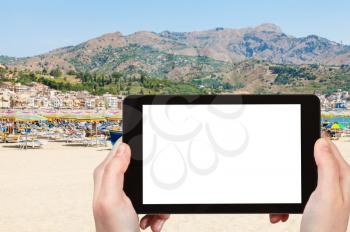 travel concept - tourist photographs city sand beach in Giardini-Naxos town in Sicily Italy in summer day on tablet with cut out screen for advertising logo