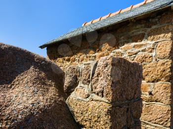 travel to France - granite boulder and wall of breton stone house in Ploumanac'h site of Perros-Guirec commune on Pink Granite Coast of Cotes-d'Armor department of Brittany in sunny summer day