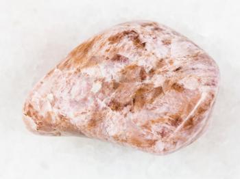 macro shooting of natural mineral rock specimen - tumbled Ussingite gemstone on white marble background from Punkaruayv mine, Lovozero Massif, Kola Peninsula, Russia