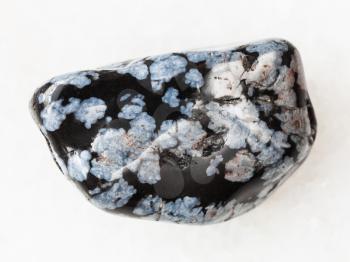 macro shooting of natural mineral rock specimen - polished snowflake obsidian gem stone on white marble background from USA