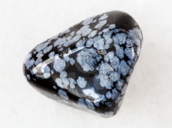 macro shooting of natural mineral rock specimen - pebble of snowflake obsidian gem stone on white marble background from USA