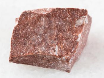 macro shooting of natural mineral rock specimen - piece of rough red marble stone on white marble background