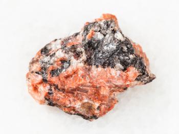 macro shooting of natural mineral rock specimen - raw red granite stone on white marble background